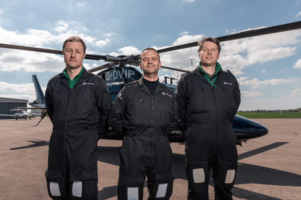 Three of the plant health team stand in a line facing the camera in front of a helicopter